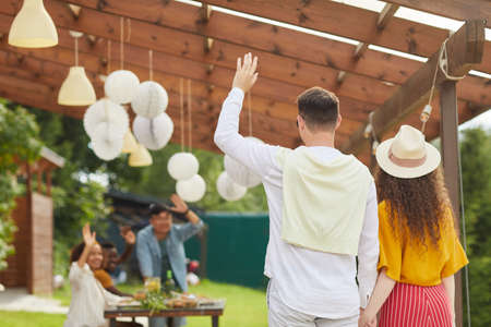 Back view portrait of young couple waving to friends while leaving outdoor party in Summer, copy spaceの写真素材
