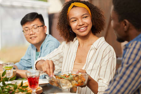 Portrait of smiling African-American woman sharing food while enjoying dinner with friends and...