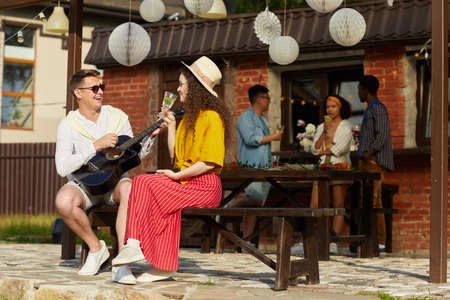 Wide angle portrait of young people enjoying outdoor party in Summer with focus on man playing...