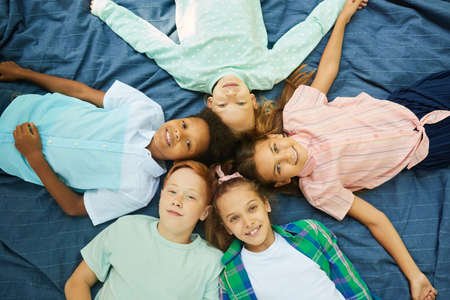 Top view at multi-ethnic group of kids lying in circle on blanket outdoors and looking at cameraの写真素材