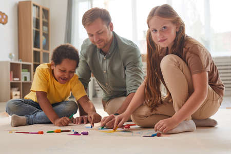Full length portrait of young male teacher working with smiling kids while having fun in preschool...