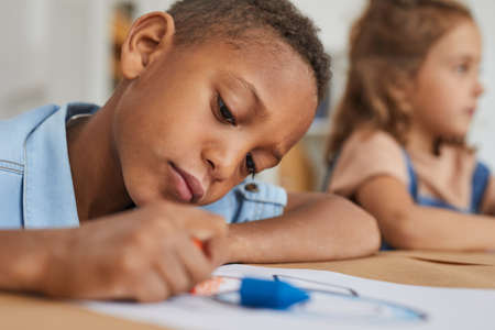 Close up portrait of African-American boy drawing pictures with crayons while enjoying art class in...