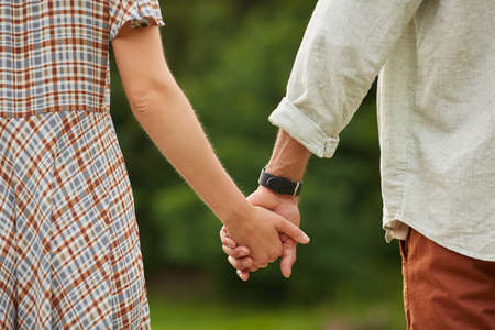 Close up of romantic adult couple holding hands in rustic countryside scenery, copy space