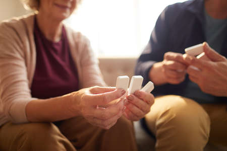Warm toned close up of unrecognizable senior couple holding domino pieces while playing board games...