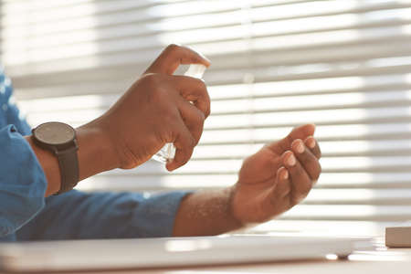 Side view close up of unrecognizable African-American businessman spraying hands with sanitizer at...