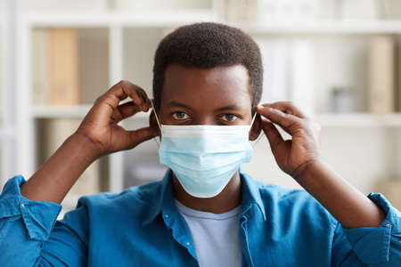 Head ad shoulders portrait of young African-American man putting on face mask while working in post...