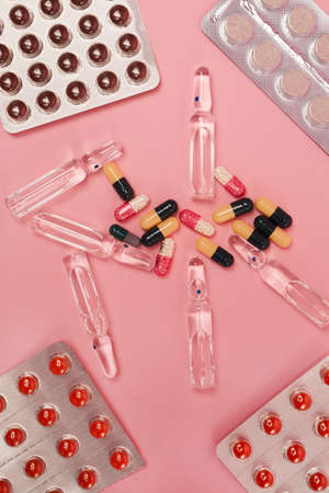 Vertical top down view at flat lay of medicine capsulles, pills and thermometer on pink background,...