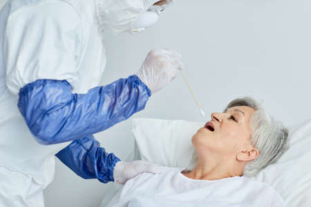Professional doctor wearing protective uniform taking senior womans swab for dangerous virus test...