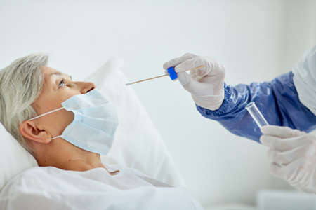 Side view close-up shot of doctor wearing protective uniform taking senior womans nasal swab for...