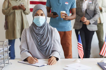 Multi-ethnic group of people standing in row and wearing masks at polling station on election day,...