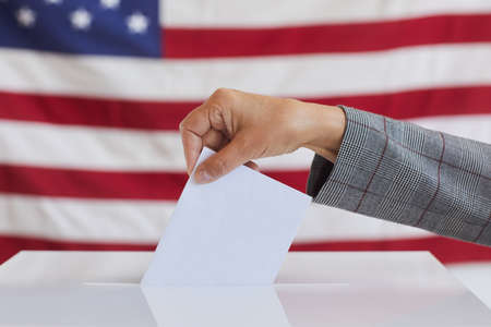Side view close up of unrecognizable woman putting vote bulletin in ballot box while standing...