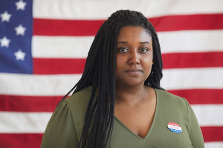 Head and shoulders portrait of young African-American woman with VOTE sticker looking at camera...