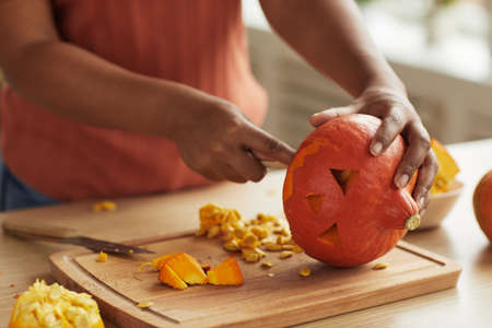 Unrecognizable modern young African American woman carving small pumpkin for Halloween decorationの写真素材