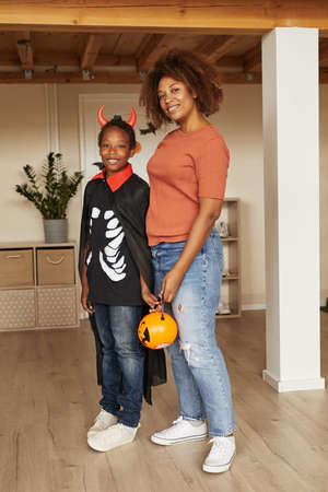 Vertical full shot of modern woman and her son wearing little devil costume standing together looking at cameraの写真素材