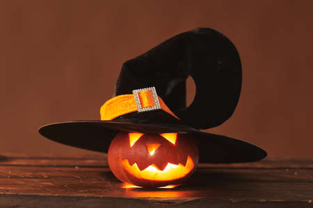 Close-up studio shot of cute Jack O Lantern wearing black witch hat with candle glowing inside of it, brown backgroundの写真素材