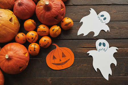 Top-down flat lay shot of carved ripe pumpkins, tangerines and paper jack o lantern with ghosts...