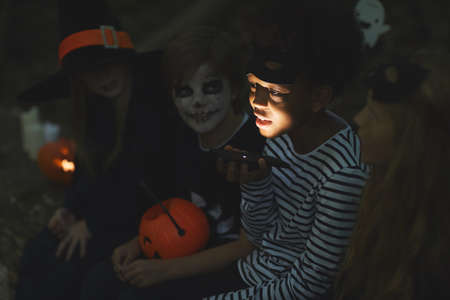 Multi-ethnic group of kids telling scary stories on Halloween, focus on African-American boy holding flashlight in foregroundの写真素材