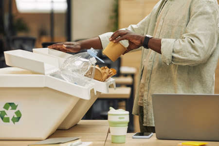 Cropped portrait of unrecognizable African-American man putting paper cup into waste sorting bin in office, copy spaceの写真素材