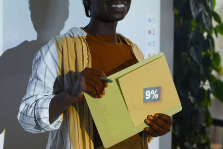 Cropped portrait of smiling African-American woman giving presentation while standing by projector screen with focus on 9 percent number, copy spaceの写真素材