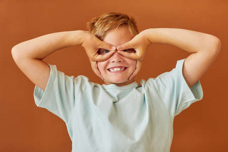 Waist up portrait of blonde teenage boy making faces at camera and posing like a superhero while...