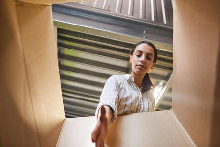 Low angle POV shot at young woman reaching into box while loading self storage unit, copy space