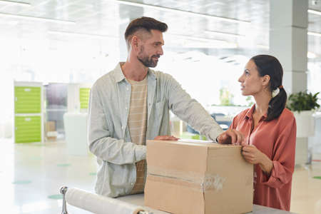 Waist up portrait of adult couple looking at each other while packing cardboard boxes in storage...