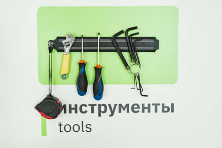 Background image of magnetic tool rack with wrenches and screwdrivers over word TOOLS written in English and Russianの写真素材