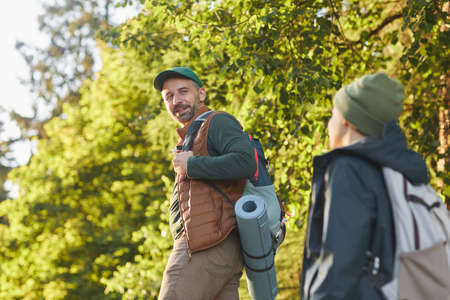 Portrait of happy father and son hiking together and talking while walking in forest with backpack, copy spaceの写真素材