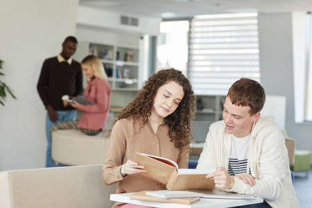 Portrait of two young students boy ad girl studying together while sitting at table in college...