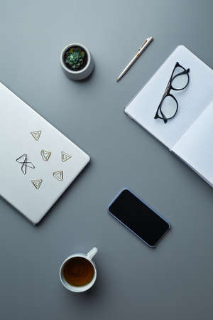 Above view flat lay of smartphone and blank planners on grey workplace background with coffee cup...