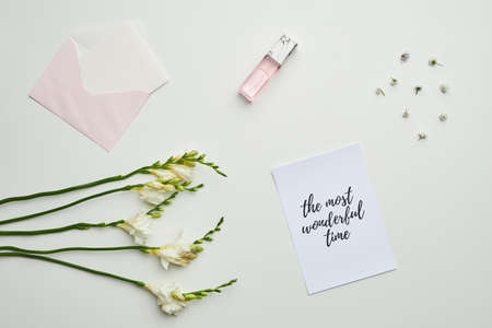 Minimal background composition of envelope and perfume on table with floral details and lettering the most wonderful time, copy spaceの写真素材