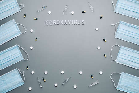 Above view composition of medical masks framing coronavirus word and medication laid out over grey background, copy spaceの写真素材