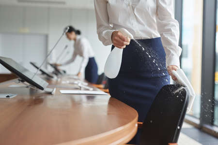 Cropped shot of elegant young women cleaning conference room with sanitizing spray while preparing...
