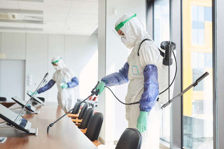 Side view portrait of two workers wearing hazmat suits disinfecting conference room in office, copy spaceの写真素材