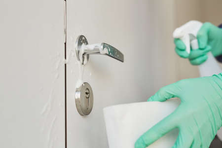Close up of unrecognizable sanitation worker wearing gloves cleaning door handles with disinfecting...
