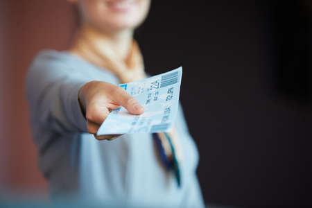 Close up of unrecognizable female flight attendant handing tickets to passenger while standing at check in desk in airport, copy spaceの写真素材