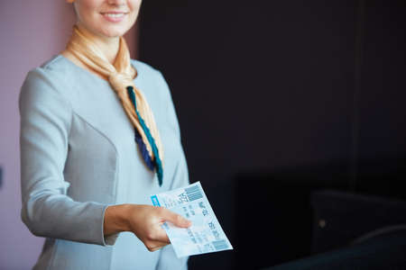 Cropped portrait of smiling flight attendant handing tickets to passenger while standing at check in desk in airport, copy spaceの写真素材