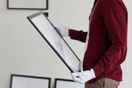 Cropped portrait of unrecognizable man wearing gloves holding painting frame while standing against...