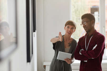 Waist up portrait of female art gallery manager instructing assistant while planning exhibition in museum, copy spaceの写真素材