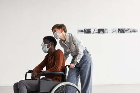 Minimal portrait of African-American man using wheelchair and looking at paintings in modern art...