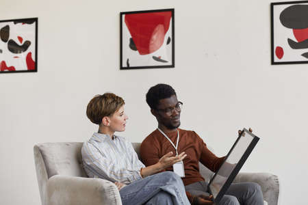 Portrait of African-American man talking to female art gallery manager while discussing paintings...