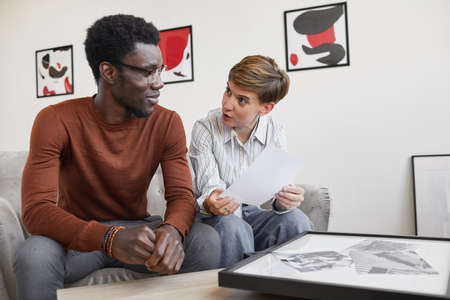 Portrait of African-American man talking to female art gallery manager while discussing paintings...