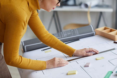Cropped side view portrait of unrecognizable female architect drawing blueprints while leaning on...