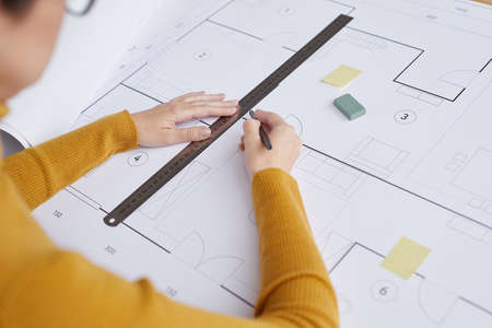 High angle close up of female architect drawing blueprints and plans while sitting at desk in...