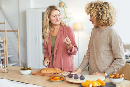 Waist up portrait of two young women chatting happily while cooking for dinner party indoors, copy spaceの写真素材
