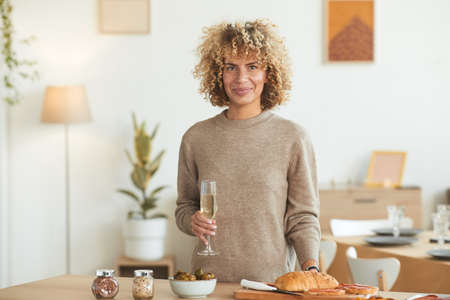 Waist up portrait of contemporary mixed-race woman holding champagne glass and looking at camera...