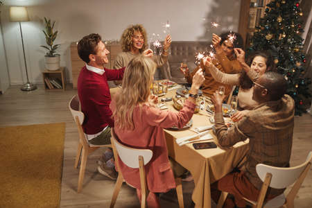 Wide angle view of people toasting with champagne glasses while enjoying dinner party at Christmas...