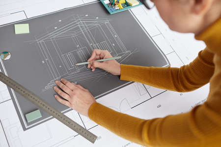 High angle shot of unrecognizable female architect drawing blueprints and plans while working at...