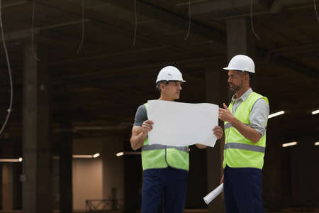 Portrait of two building contractors discussing plans while standing on industrial construction...
