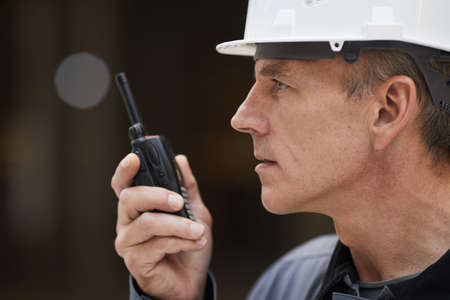 Side view portrait of mature worker speaking by walkie-talkie while supervising work at construction...